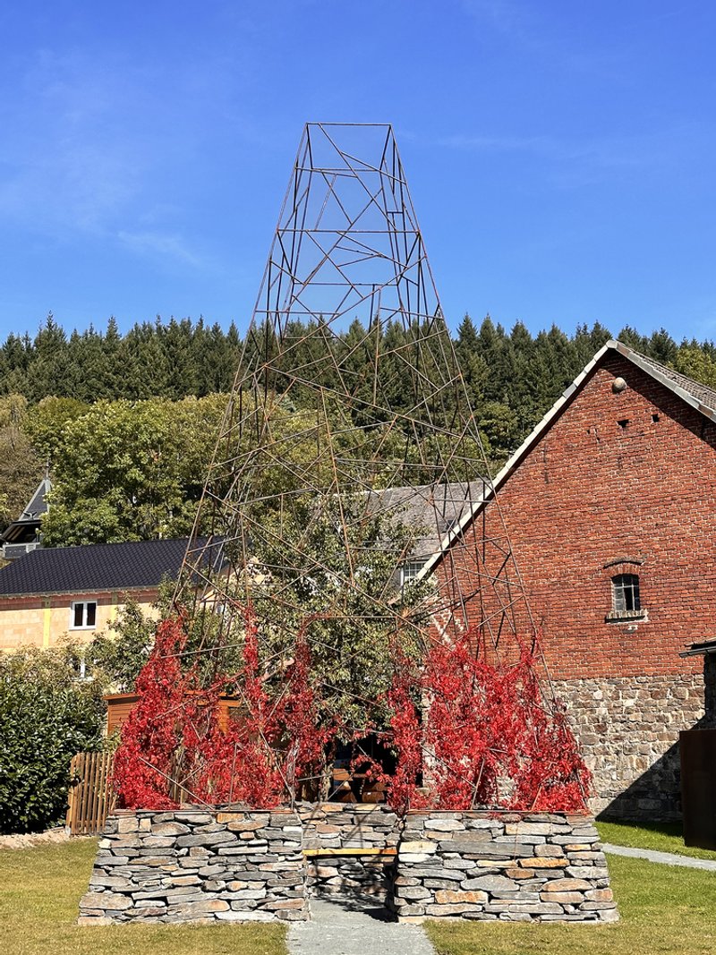 Circular slate stone bench surrounding a bare tree with autumn foliage and brick barn beyond