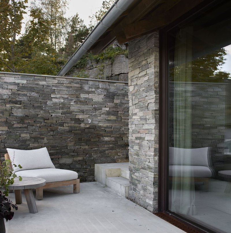 Exterior terrace with concrete floor and stacked stone wall enclosing seating beneath a metal roof