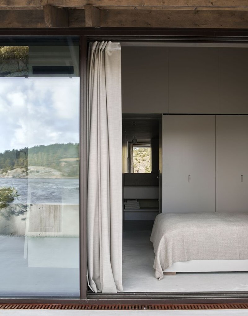 Bedroom with floor-to-ceiling glazing, linen curtain and view toward the forested waterfront