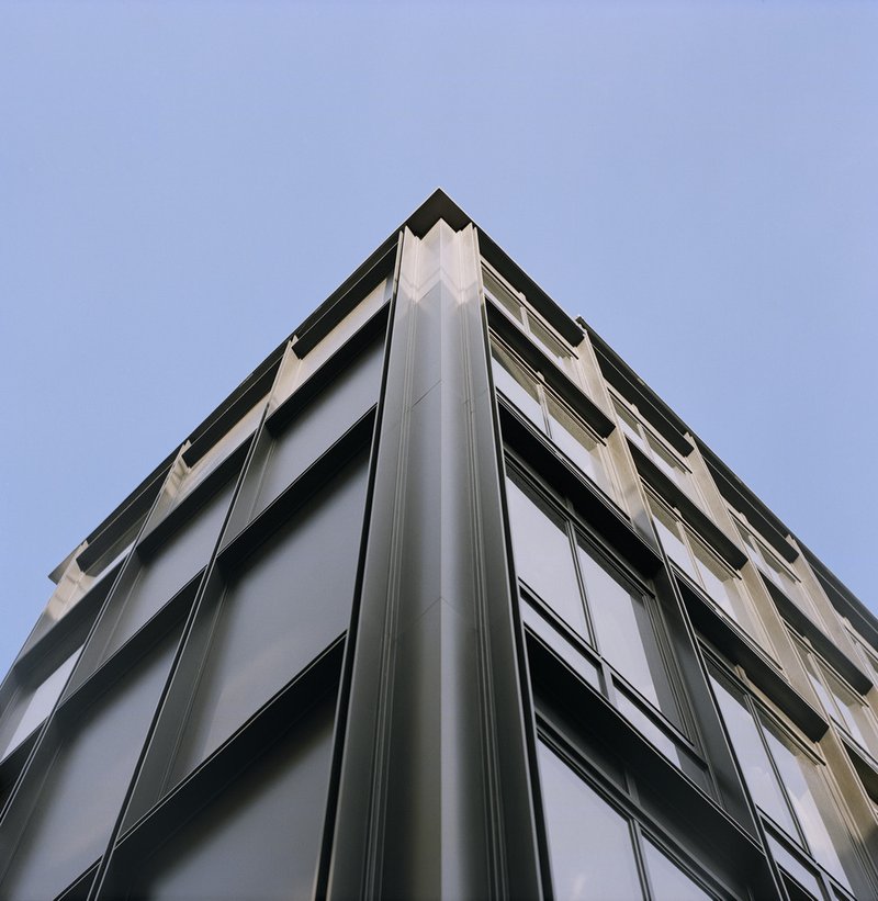 Upward view of metal-clad corner facade with horizontal window bands against pale sky