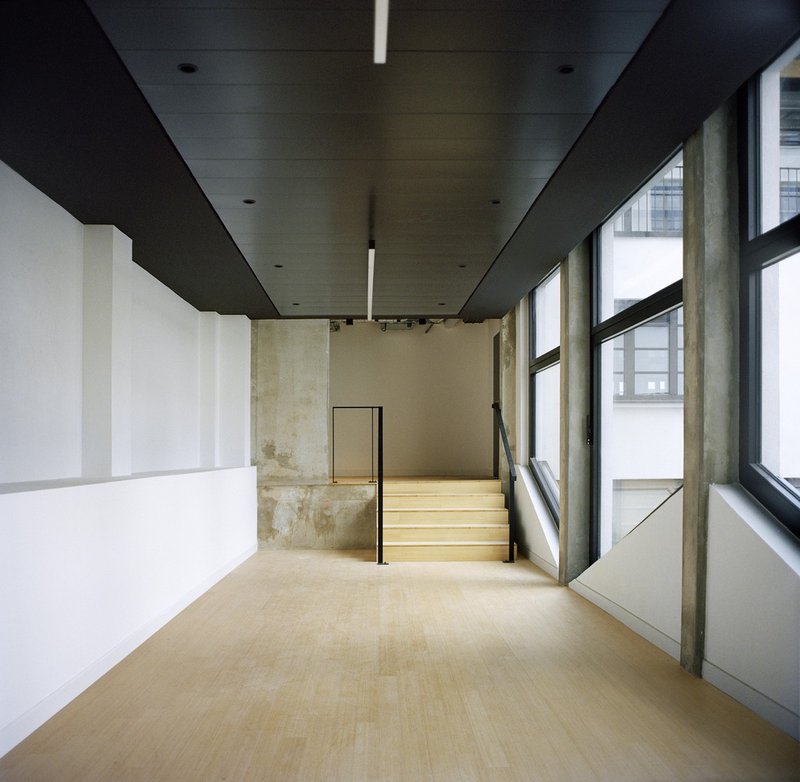 Interior hallway with black ceiling plane and timber staircase ascending alongside floor-to-ceiling windows
