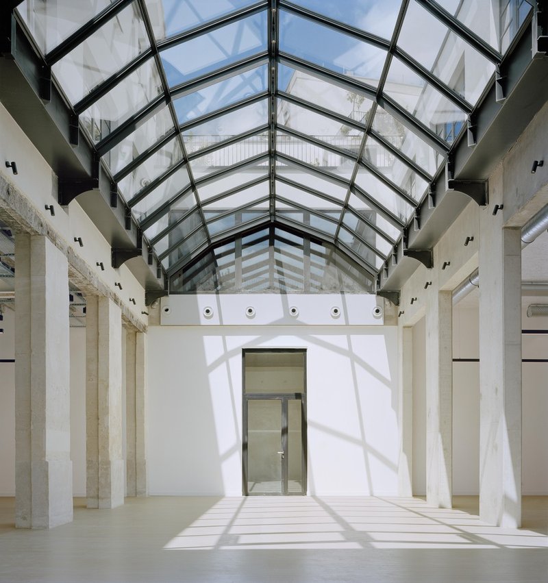 Central atrium with gabled glass roof casting shadows on concrete columns and pale flooring