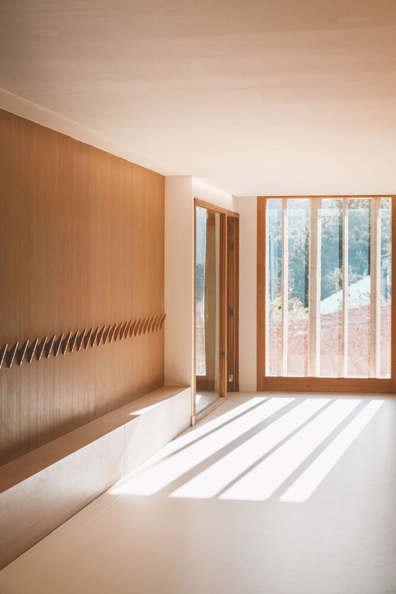 Interior space with oak wall and timber-framed glazing casting striped shadows across white resin floor