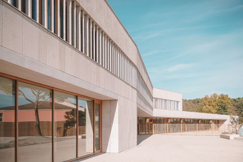 Curved precast concrete facade with vertical brise-soleil above timber-framed glazing and exterior terrace