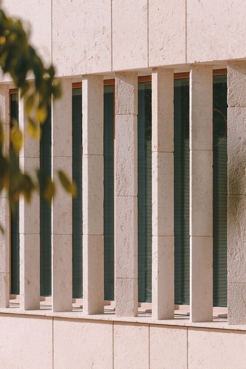 Facade detail with vertical green louvered vents set between stone panels in sunlight