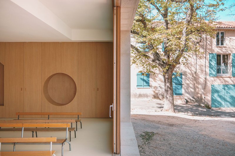 Interior view through doorway with circular timber wall panel and benches facing a courtyard tree