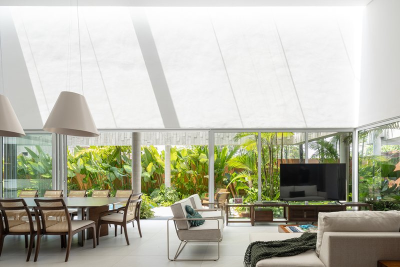 Open living and dining space with sloped skylight casting linear shadows above floor-to-ceiling garden windows