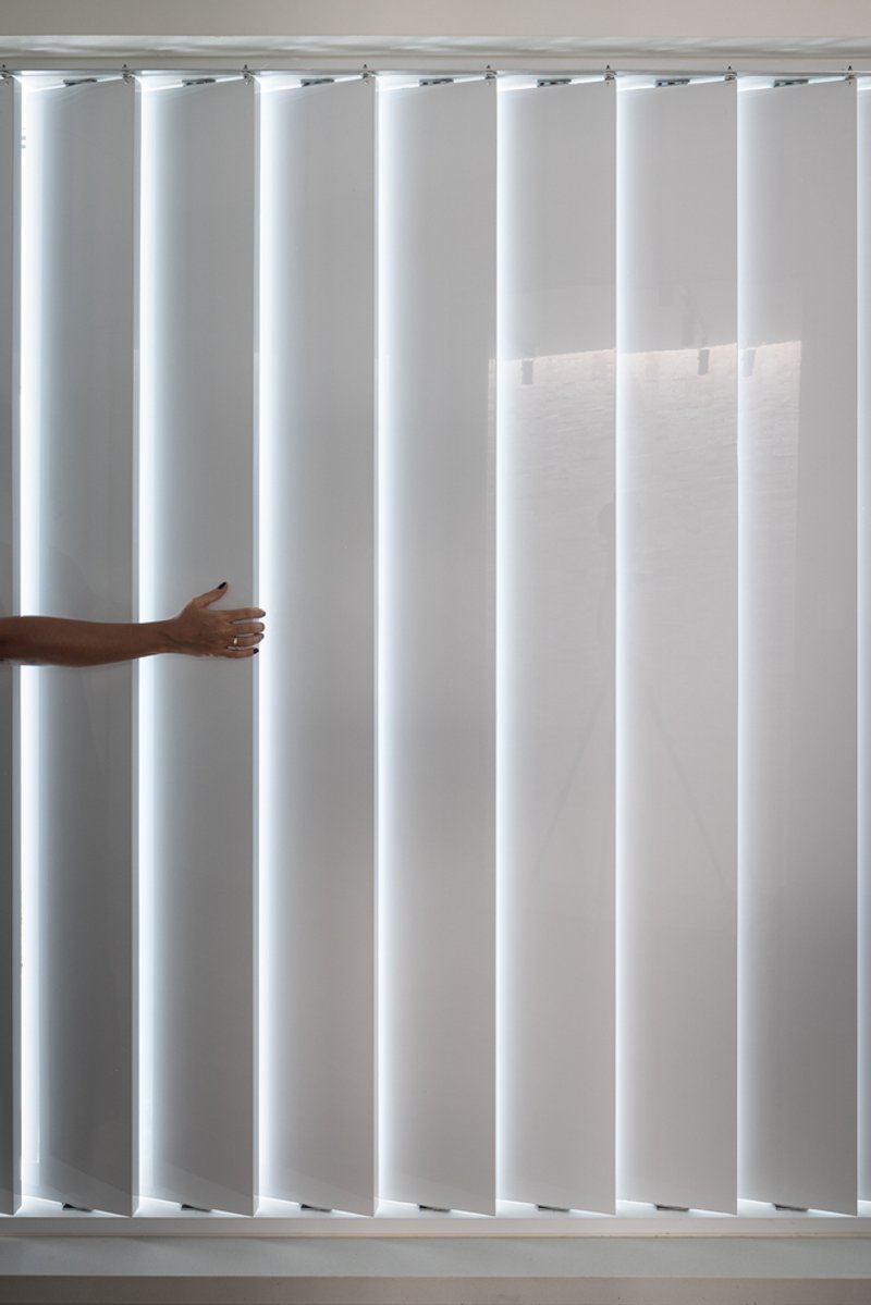 Vertical louver blinds with hand pulling one panel to adjust interior daylight