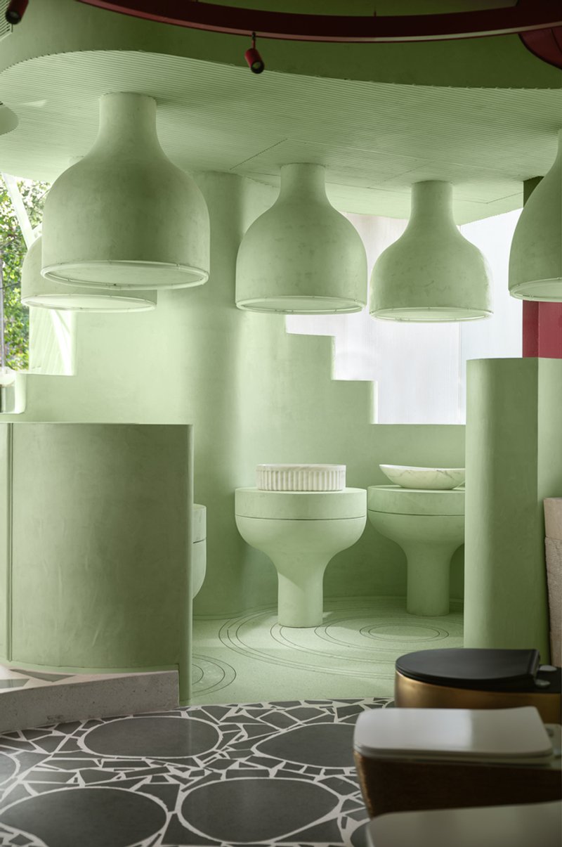 Row of large bottle-shaped pendant lights suspended above pale green partition walls with natural light visible beyond