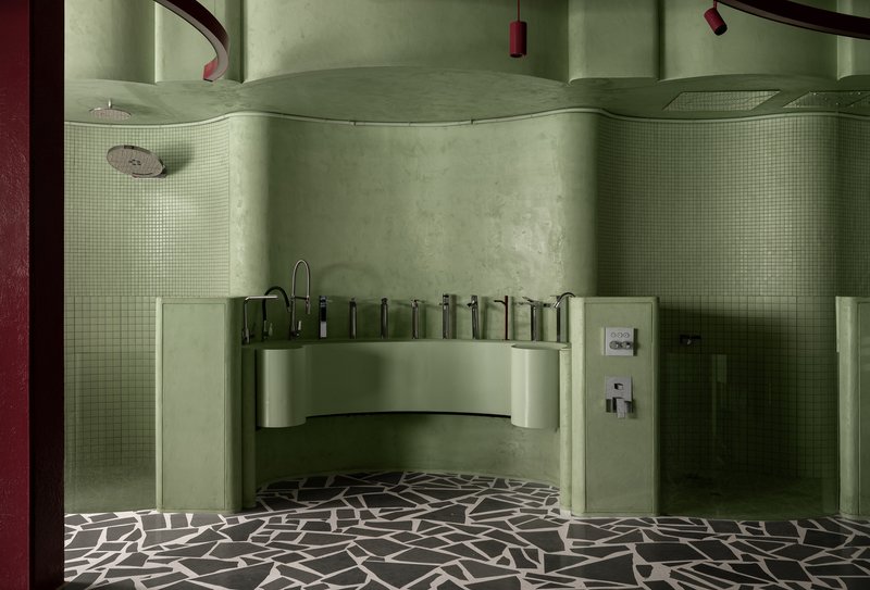 Curved vanity counter with multiple faucets flanked by tile-clad shower enclosures and terrazzo flooring