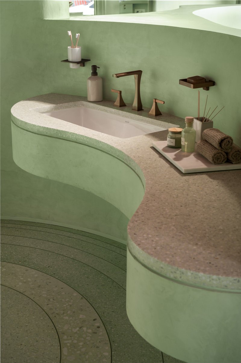 Curved vanity with integrated sink and terrazzo countertop against soft green plaster walls