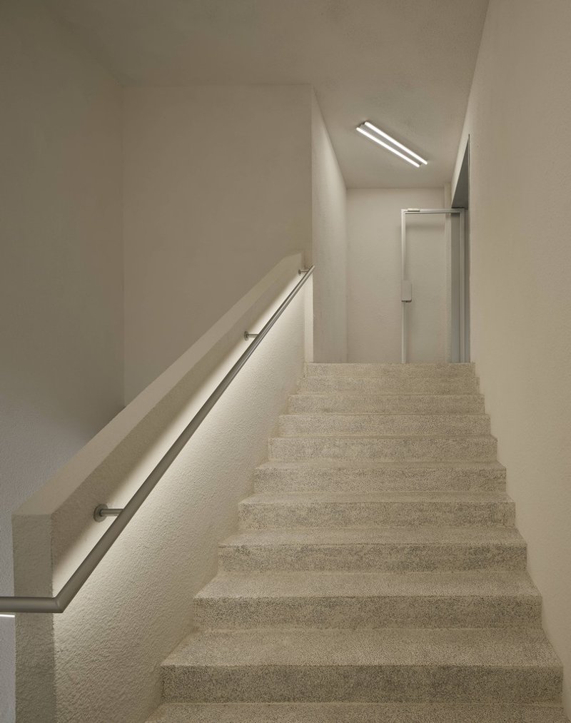 Terrazzo staircase ascending toward skylight with metal handrail and recessed linear illumination
