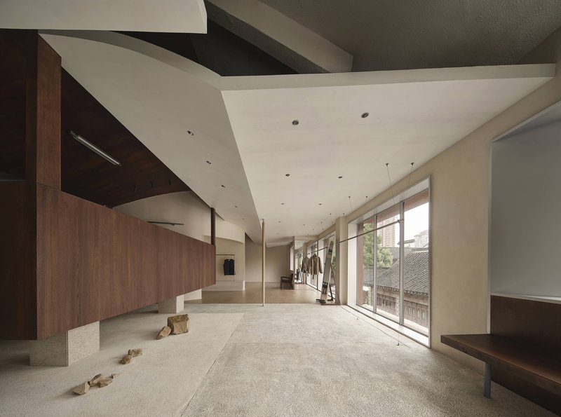 Double-height interior space with folded plaster ceiling, timber walls and scattered rocks on terrazzo flooring
