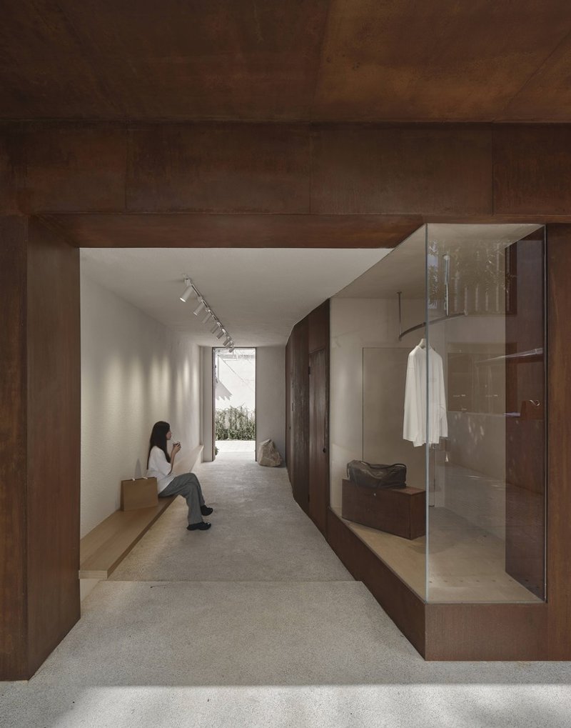 Timber-clad corridor with built-in bench seating and glazed display niche, a visitor seated in afternoon light