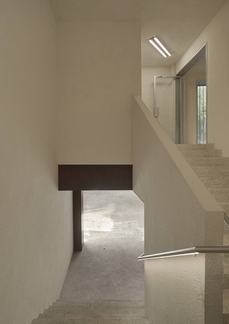 Stairwell with timber beam framing a low passage and daylight filtering through upper skylights