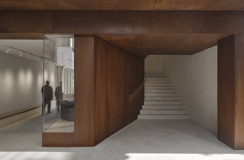 Stone staircase ascending beside dark walnut volume with glass retail partition revealing visitors inside