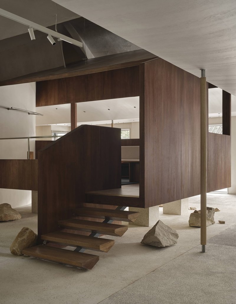 Cantilevered walnut-clad volume with floating treads and large stone boulders on polished terrazzo floor