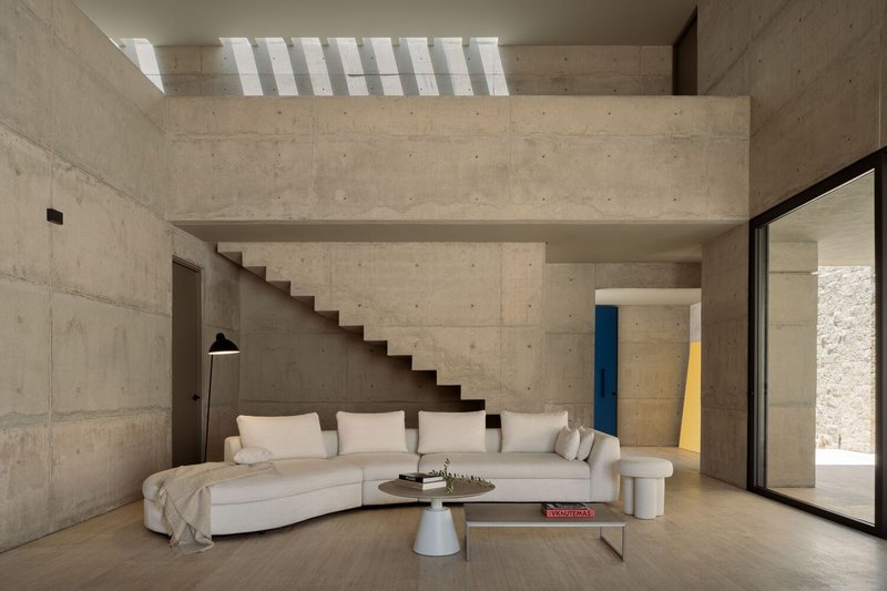 Double-height living room with cantilevered concrete staircase beneath a slatted skylight casting shadow stripes
