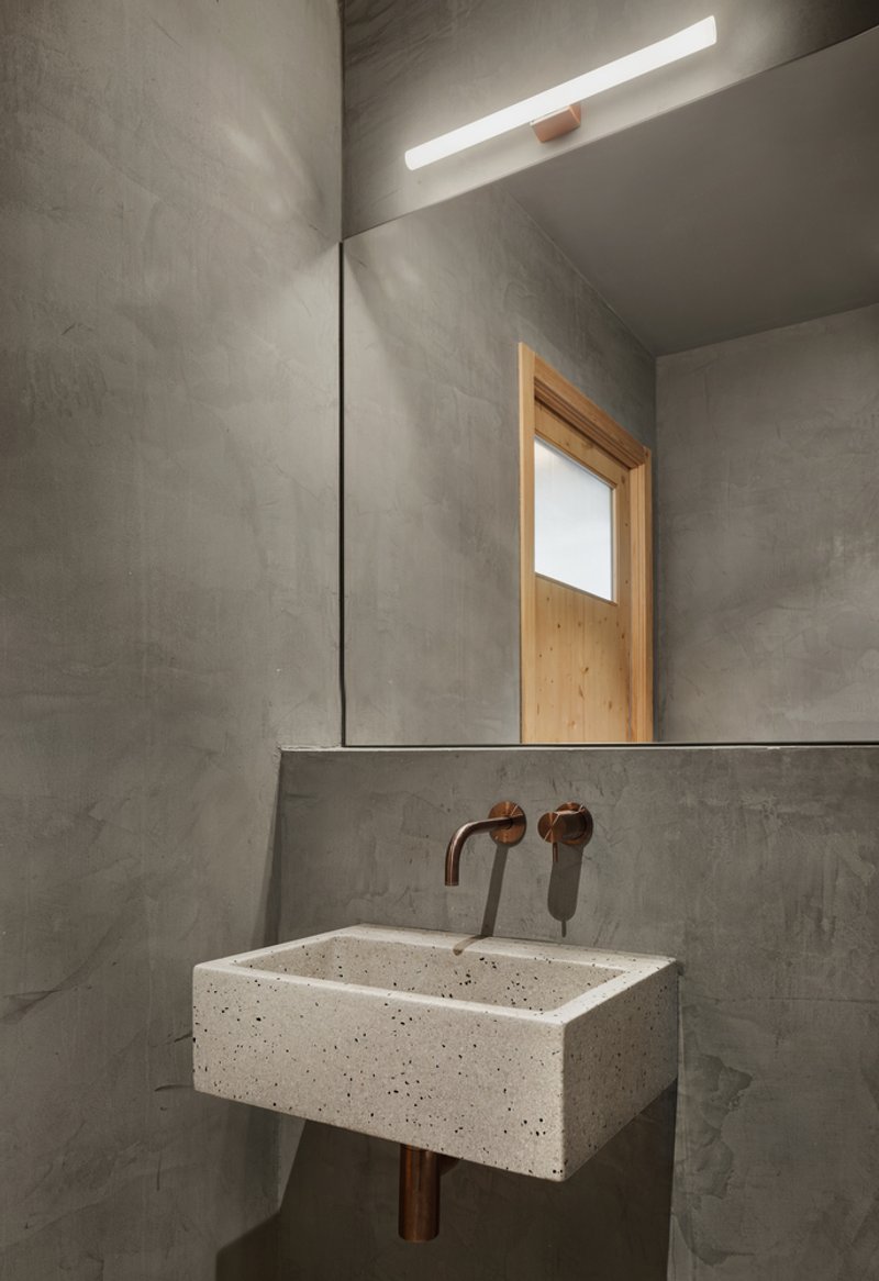 Powder room with cast concrete walls, terrazzo basin and copper fixtures under a skylight