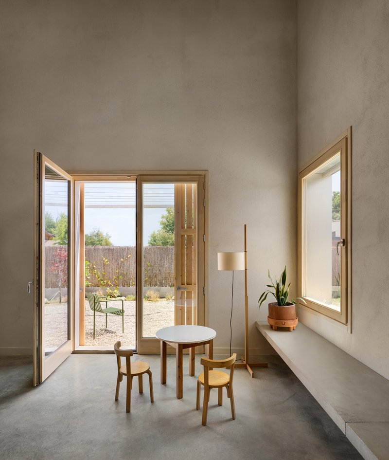 Glazed door opening to gravel courtyard with reed fence and a single round table with two stools
