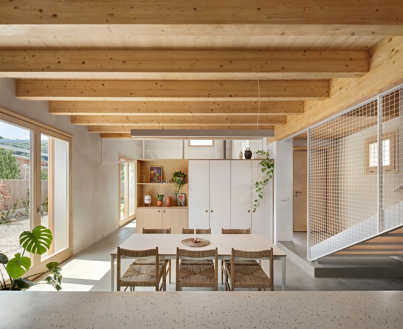 Open-plan dining space with exposed timber beams and mesh partition wall in daylight