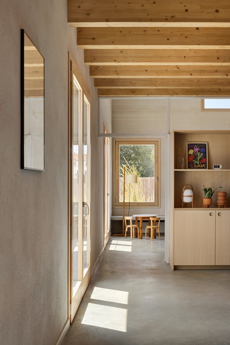 Sunlit hallway with concrete floor and timber-framed glazing casting shadows across the passage
