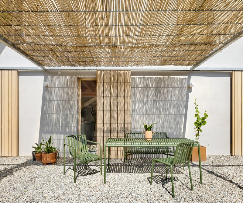 Covered courtyard with woven reed canopy over green metal dining furniture on gravel