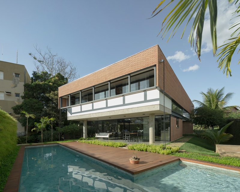 Two-story brick facade with cantilevered upper volume above pool and timber deck under palm trees