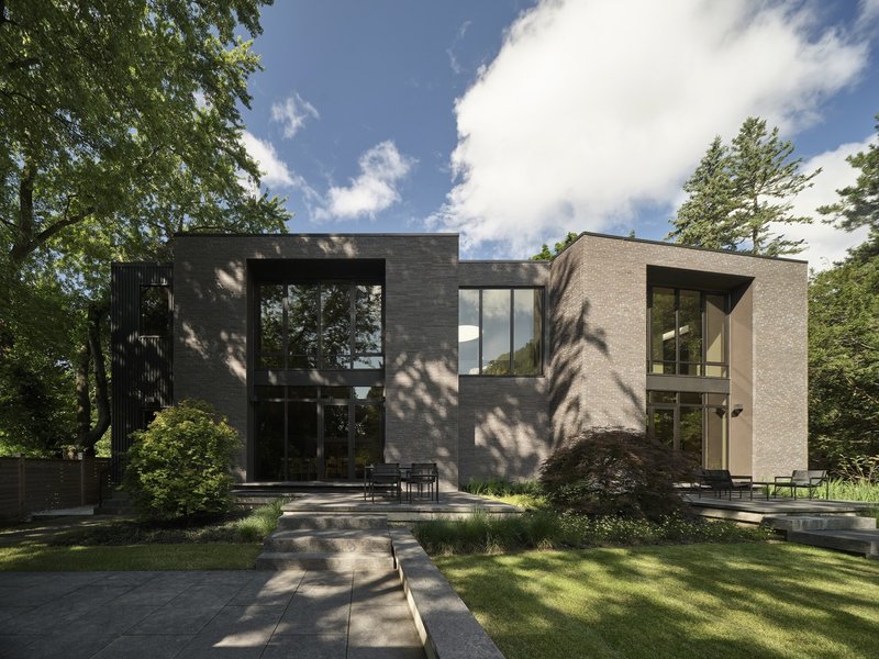 Garden elevation showing pale brick and dark metal volumes framed by tree shadows and lawn
