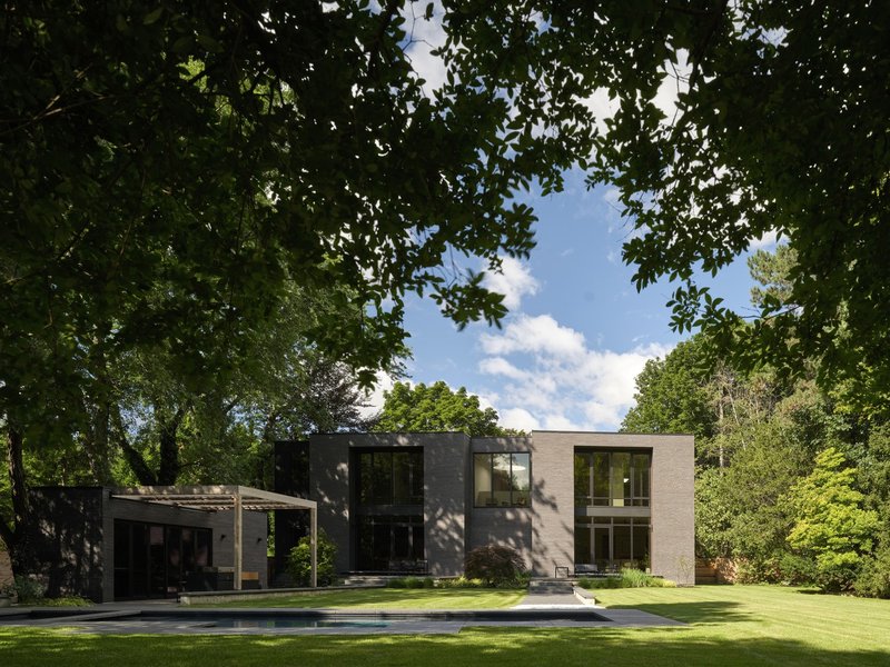 Rear facade across lawn showing contrasting dark and light brick volumes beneath summer foliage