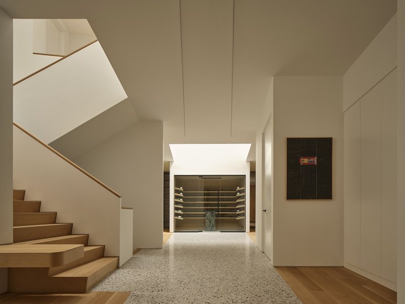 Hallway with terrazzo floor looking toward the backlit wine cellar and timber staircase beyond