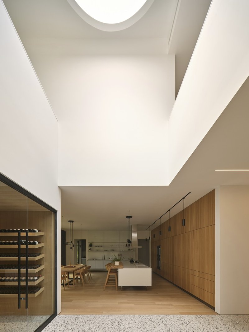 Double-height kitchen space with circular skylight above timber cabinetry and terrazzo flooring