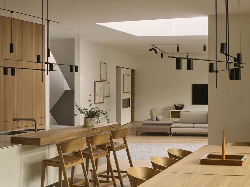 Open-plan interior with timber dining bar and suspended track lighting beneath a rectangular skylight