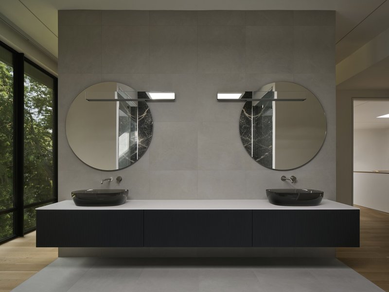 Floating bathroom vanity with twin black basins below paired circular mirrors and marble wall sconces