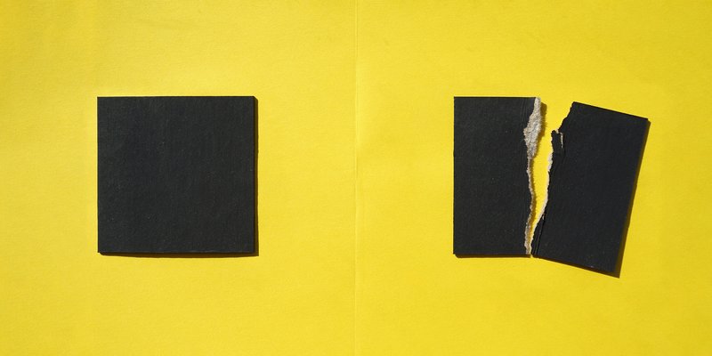 Close-up of yellow wall surface with two black square openings showing torn edges
