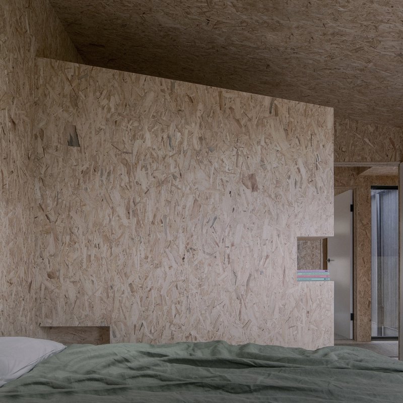 Bedroom with oriented strand board walls and ceiling featuring a recessed storage niche above the bed