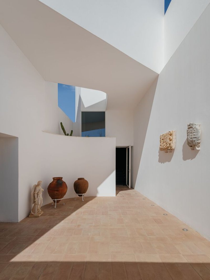 Interior courtyard with white stucco walls displaying terracotta urns and carved stone reliefs beneath geometric skylights
