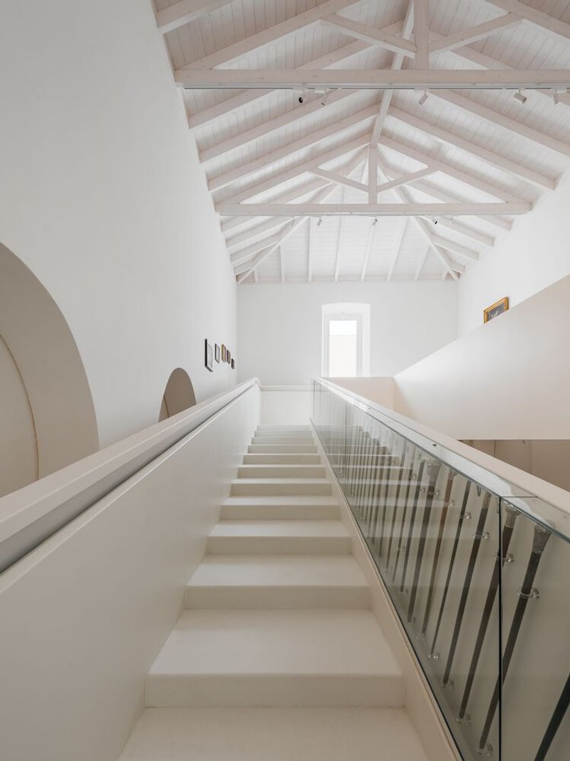 Staircase rising toward exposed timber roof structure with central skylight above white plastered walls