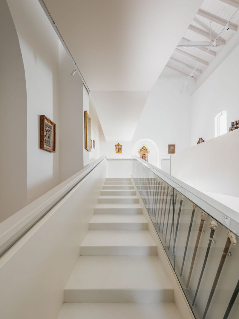 Upward view of staircase with glass railing leading toward window beneath whitewashed timber roof trusses