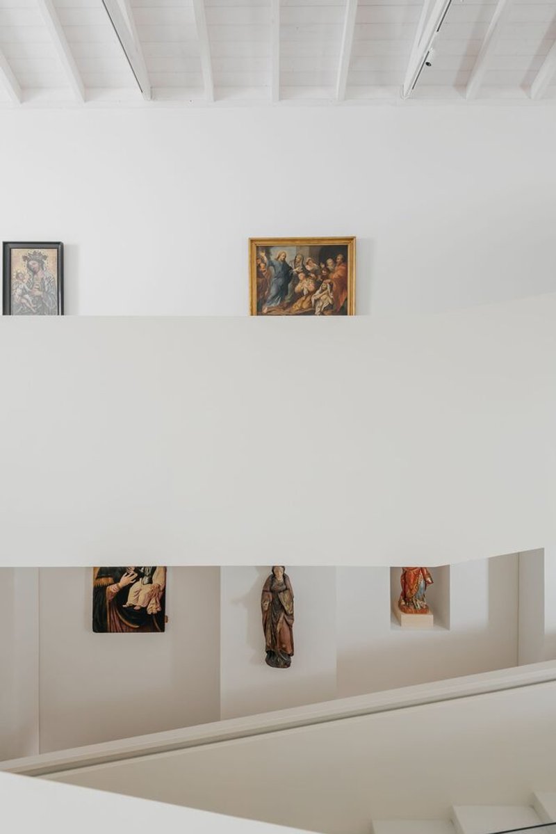 View across gallery levels showing white parapet walls with displayed artworks and sculptures in niches below
