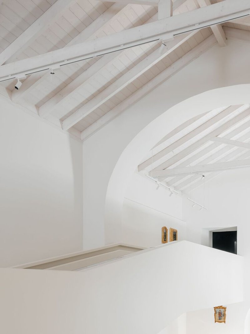 Detail of intersecting white barrel vaults with exposed timber roof rafters and track lighting mounted above