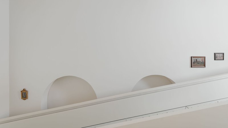 White plastered wall with arched alcoves and framed artworks hung at intervals