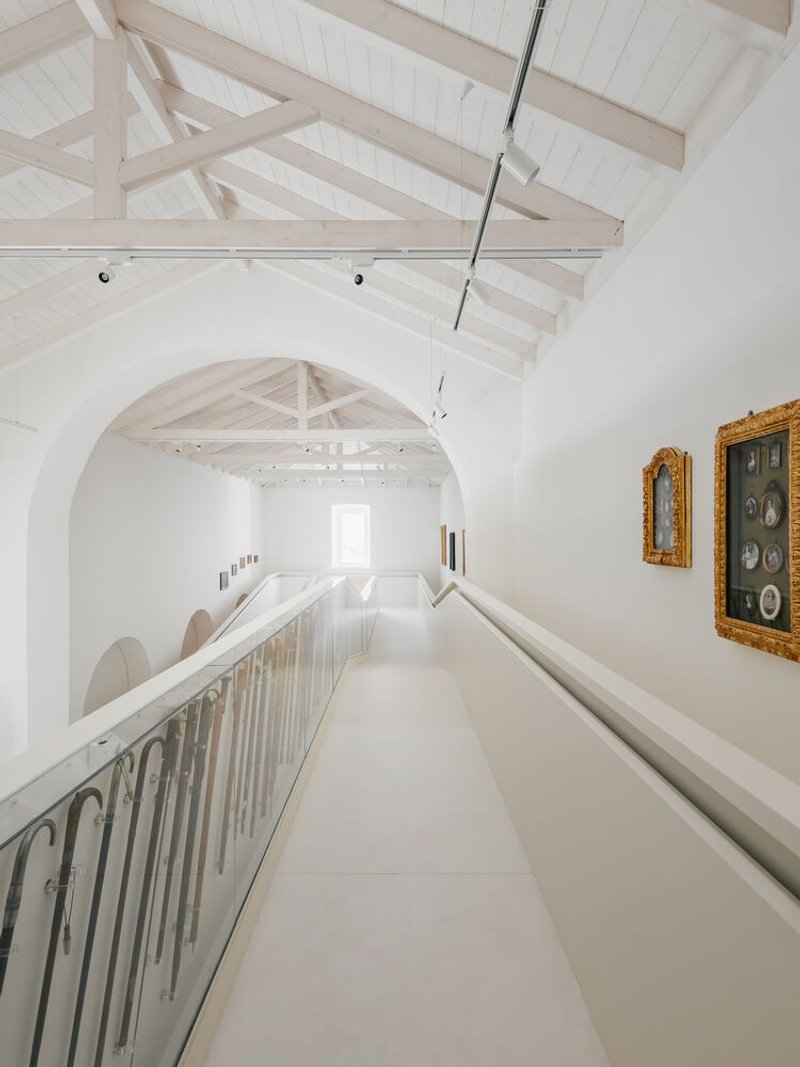 Upper gallery walkway with metal balustrade and artworks on the white wall