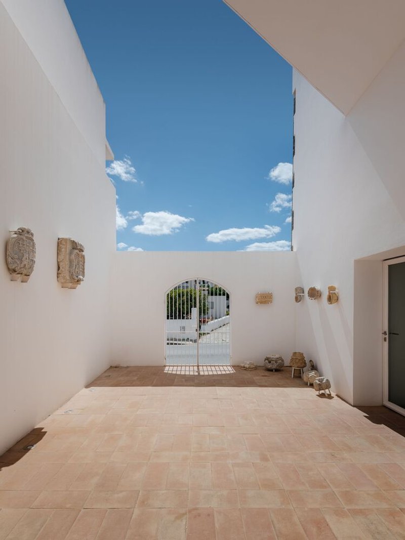 Roofless courtyard with terracotta pavers and stone fragments on walls framing a distant gate