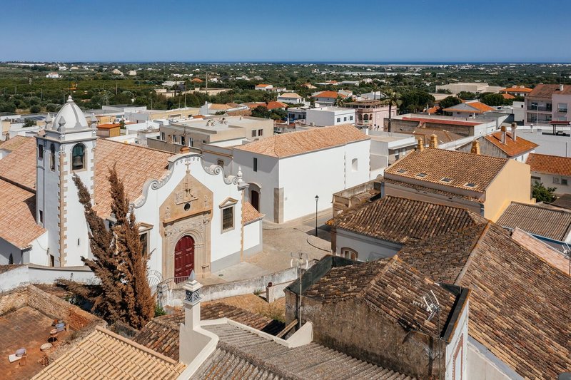 Elevated view of a white church with bell tower and terracotta rooftops in a low-rise town