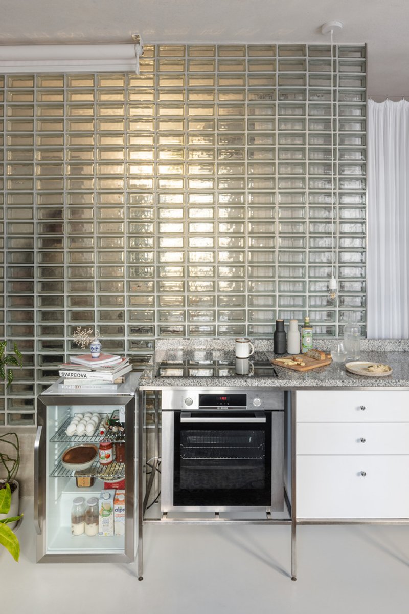 Kitchen counter with oven and mini fridge below a full-height glass block wall glowing with daylight