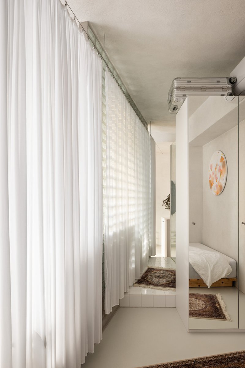 Floor-to-ceiling sheer curtain beside a glass block wall with a white column framing the bedroom beyond