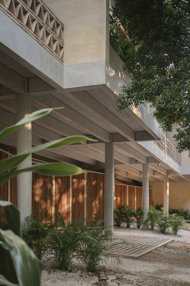 Covered entry colonnade with exposed timber beams and vertical wood screens lit by warm afternoon light