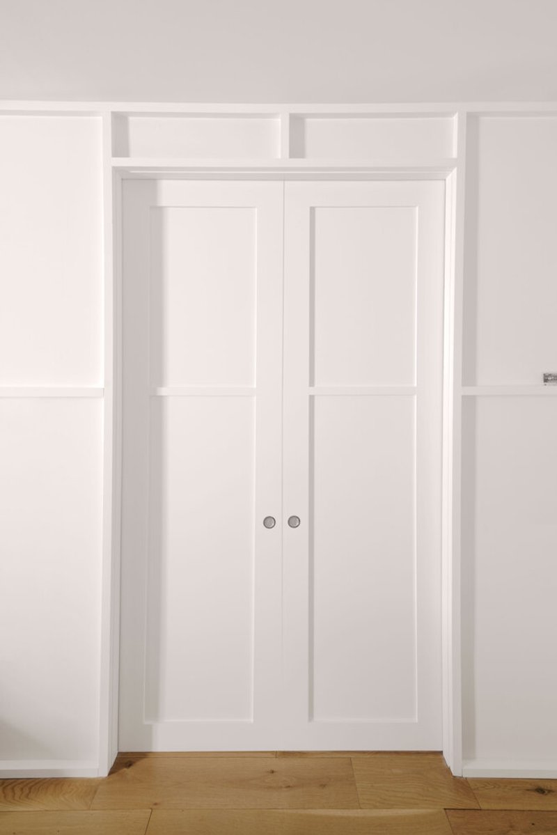 White paneled closet doors with twin handles set into recessed millwork and oak flooring
