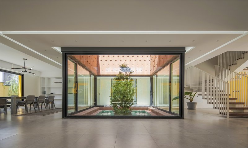 Interior view through black-framed glazing toward the timber-clad courtyard roof with perforated skylight panels